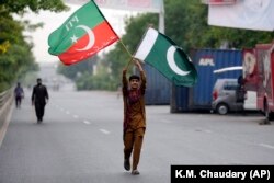 په لاهور کې یو هلک د عمران خان له کور سر نېږدې د پاکستان او د تحریک انصاف ګوند بیرغونه په لاسونو کې نیولي دي - د مې ۱۷مې انځور.