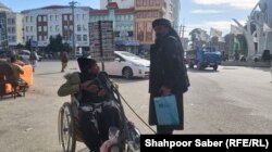 یک مرد کهنسال و معلول که در هرات روی جاده ها کارت های موبایل می فروشد