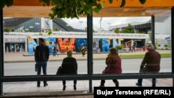 Qytetarë duke pritur në një stacion autobusësh përballë obeliskut të pavarësisë NEWBORN në Prishtinë, maj 2024.