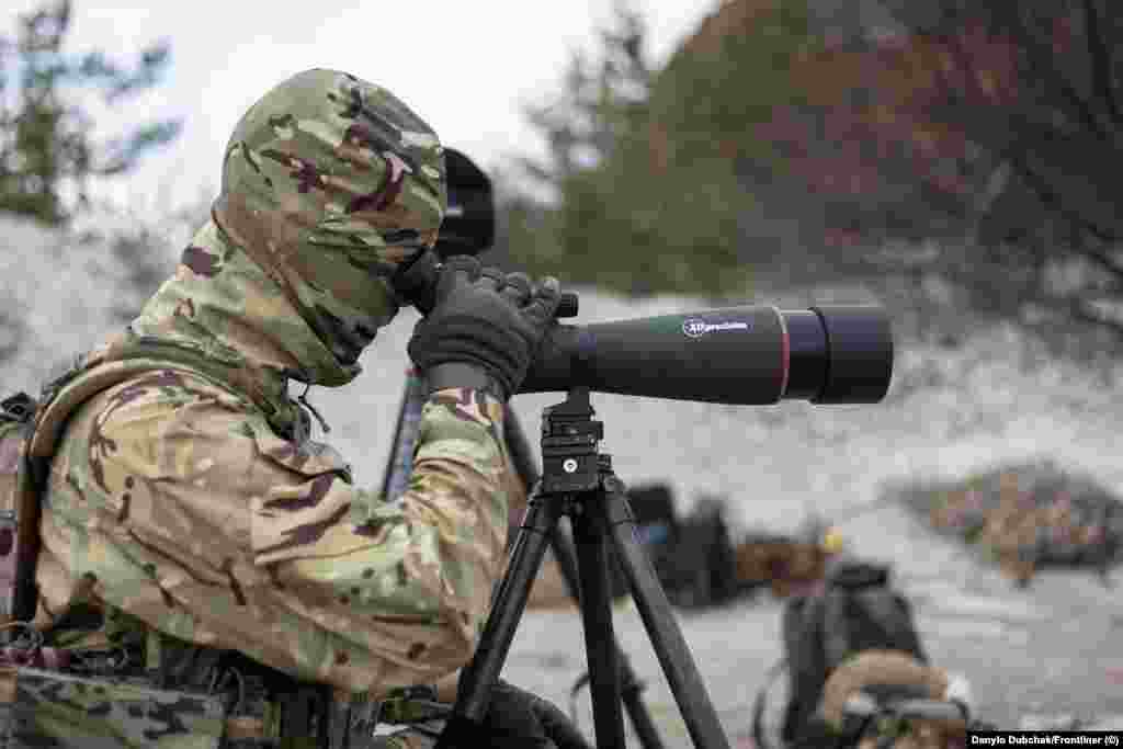 Un instructor urmărește tragerea la țintă. Pregătirea la Alpha Bravo include trageri pe timp de noapte cu ajutorul lunetei infraroșu. Având un buget limitat pentru a simula țintele inamice calde, instructorii aprind un mic foc într-o groapă sub țintele metalice, care apoi strălucesc intens prin vizorul cu vedere nocturnă. &bdquo;Costă 50 de hrivne (1,25 dolari) o pungă de cărbune pentru grătar&rdquo;, spune Elanski. &bdquo;Și cu asta poți antrena o unitate întreagă&rdquo;.