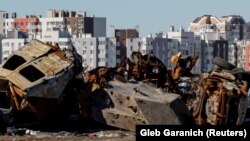 Цивільні автомобілі й військова техніка, знищені під час нападу Росії на Україну, перед житловими будинками в місті Буча, 30 березня 2023 року