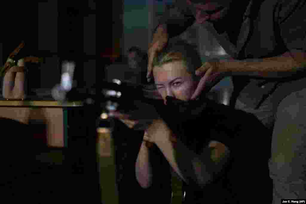 Një instruktor duke drejtuar qëndrimin e një gruaje, e cila është duke e mbajtur një pushkë AK-47 gjatë trajnimit për gjuajtje me armë zjarri. "Qëllimi kryesor këtu është që t'i mësojmë njerëzit se si të mbijetojnë dhe t'u përgjigjen këtyre kërcënimeve ushtarake që ekzistojnë", shpjegoi Shcherbyna. Autoritetet lokale po shpresojnë se kështu duke i trajnuar njerëzit, do të parandalojnë numrin e viktimave në të ardhmen.