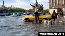 په کابل کې د ټرافیکو پولیسو یو سرتېری تر سخت باران وروسته پر سړک د ګاډو تګ راتګ تنظمیوي - پخوانی انځور.