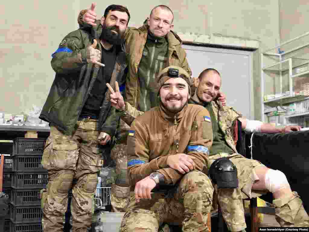 Mariupol, 2022 senesi. Merkezde - Azatlıq Radiosına bu fotoresimlerni bergen qırımlı, arbiy ekim Asan İsenacıyev. O, "Azovstal"den 2022 senesi mayıs ayında, Rusiye ordusı sarıp alğan zavodda qalğan soñki ukrayin bölükleri ile çıqtı. Bundan soñ o, diger askerlernen beraber Olenivka koloniyasına qapatıldı ve esirler ile baraknıñ patlavı vaqtında sağ qaldı. 2022 senesi dekabrniñ 31-nde Asanı deñiştirdiler. Bu fotoresimde "Vışnâ", "Şprot" ve "Grân" (soldan sağğa) arbiyler onıñnen beraber turalar. Olar sarıp alınğan Mariupolge tikuçarnen kirdiler. Olardan tek Vişnâ sağ qaldı, o da Rusiye esirliginden keçti, almaşuvdan soñ ise orduğa qayttı. Şprot ve Grân 2022 senesi baarde Mariupolde elâk oldılar