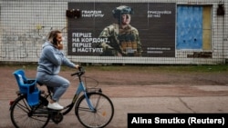 O femeie trece cu bicicleta pe lângă un anunț de recrutare pentru armata ucraineană în regiunea Dnipropetrovsk (foto de arhivă).