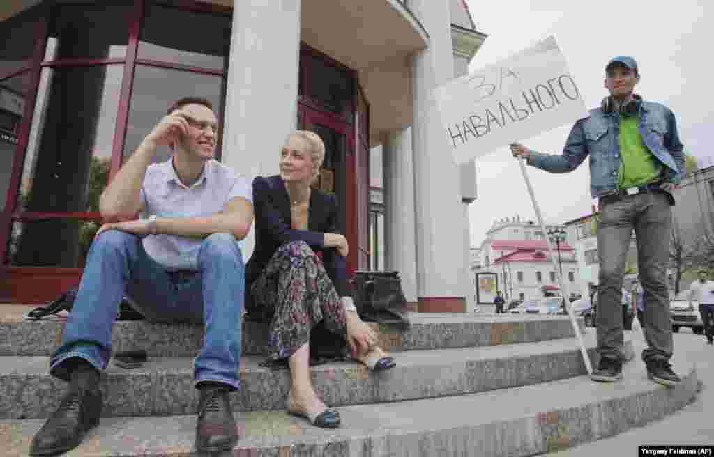 Navalny and his wife, Yulia, sit together after a court hearing as a supporter with a poster reading "For Navalny" looks on in the northwestern city of Kirov on May 16, 2013.&nbsp; Accused of embezzlement, Navalny insisted the charges were revenge for his exposure of high-level government corruption and for his campaigns against Putin.