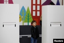 Një fëmijë duke pritur ndërsa një grua voton gjatë zgjedhjeve presidenciale në Shkup, Maqedoni e Veriut, 24 prill 2024.