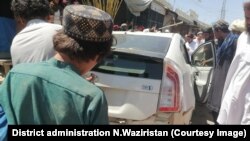 ځايي خلک په بمي برید کې د خراب شوي ګاډي خوا ته ولاړ دي ـ د جون ۲۴مې انځور.