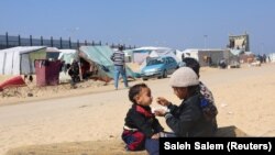 Një vajzë e zhvendosur palestineze duke e ushqyer vëllain e saj në një tendë, në qytetin jugor të Gazës, Rafah.