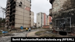 Жители на фоне фрески британского художника Бэнкси на обугленном фасаде жилого дома в Ирпене — городе недалеко от Киева, который сильно пострадал во время российского вторжения и оккупации, апрель. Автор: Сергей Нужненко, украинская редакция «Азаттыка».