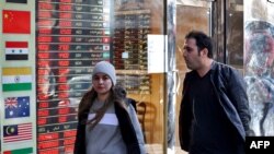 Dy persona kalojë pranë një këmbimoreje në Teheran. Sanksionet e OKB-së pritet të godasin ekonominë iraniane, përfshirë edhe dobësimin e valutës së shtetit. 