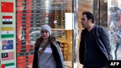 Людзі праходзяць каля пункту абмены валютаў у Тэгеране. Пасьля аднаўленьня санкцый іранскі рыял абваліўся да рэкорднага мінімуму адносна даляра на чорным рынку