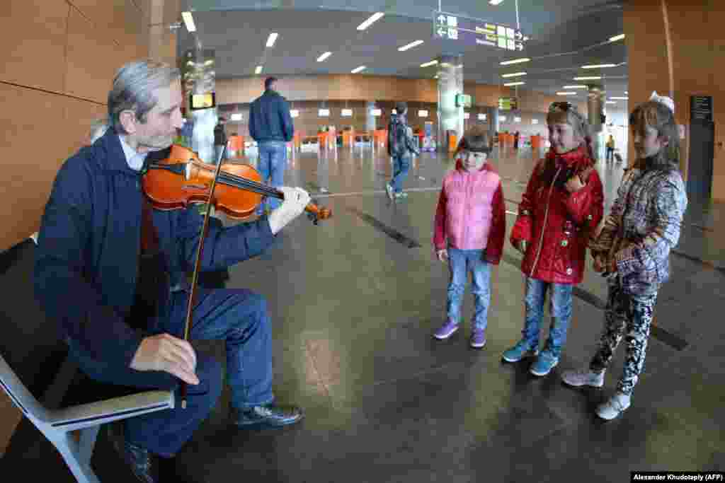 Copiii ascultă un muzician care se încălzește înainte de a cânta în aeroport, în martie 2014. La inaugurarea aeroportului, în mai 2012, viceprim-ministrul Ucrainei a prezis că noua și elegantea facilitate va „deservi aproximativ 4 milioane de pasageri pe an” până în 2015.