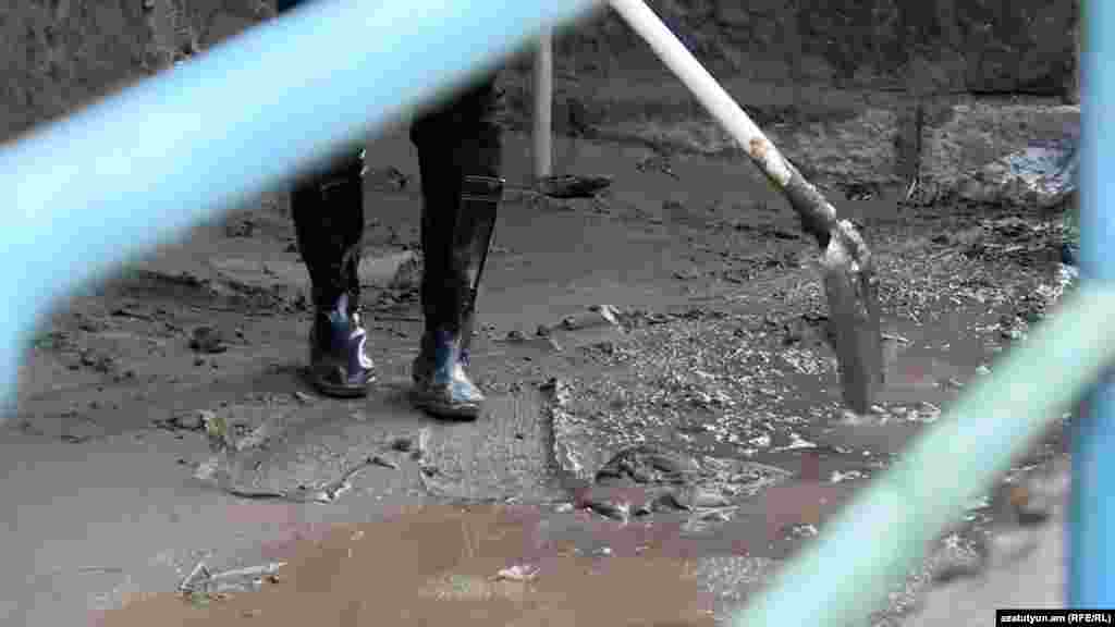 Un muncitor încearcă să curețe noroiul gros rămas în urma inundațiilor.