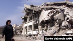 Një grua duke ecur pranë objekteve të shkatërruara diku në rajonin e Mitrovicës në vitin 2000. (Foto: AP)