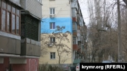 Kefede çoq qatlı binanıñ bir qısmı Ukrayina bayrağınıñ renklerine boyalanğan, 2023 senesi saban ayınıñ 17-si