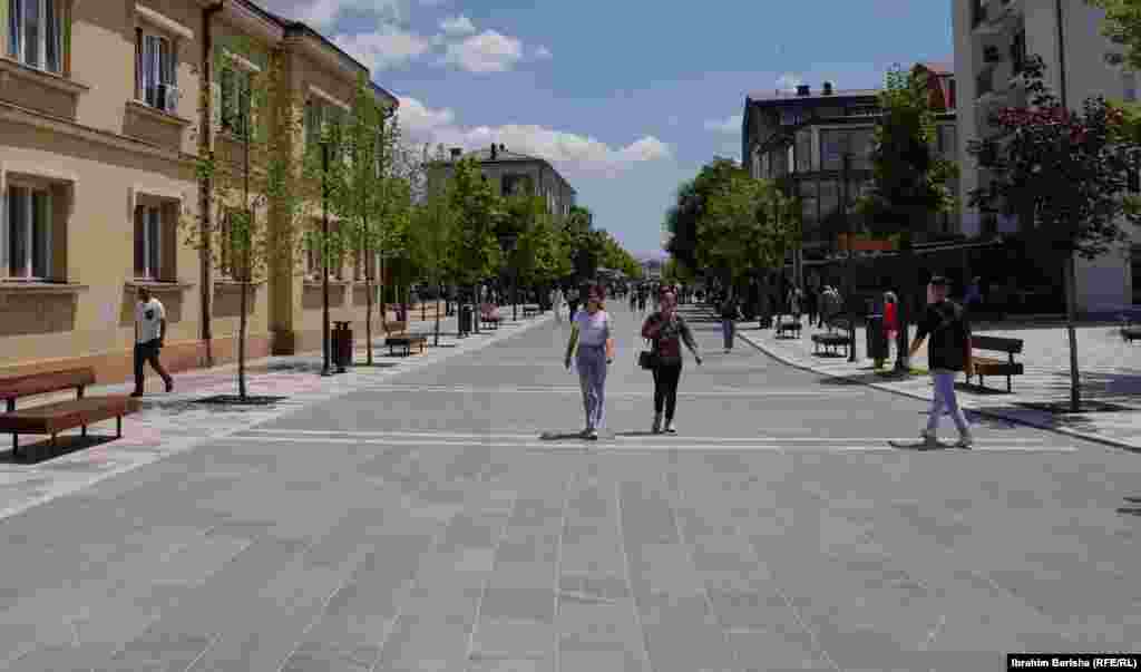 Podujevë 18 qershor 1999: Forcat e KFOR-it arritën në Podujevë disa ditë më vonë se në qytetet tjera të Kosovës. Në këtë fotografi shihen fëmijët duke vrapuar pranë një tanku derisa përshëndesin ushtarët britanikë, të cilët sapo kishin arritur në qytet. &nbsp; 6 qershor 2024: Njëzetepesë vjet pas, në të njëjtin vend objekti komunal mbetet thuajse i njëjtë. Sheshi kryesor është zgjeruar dhe janë ndërtuar objekte të reja. 