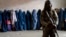 A Taliban fighter stands guard as women wait to receive food rations distributed by a humanitarian aid group in Kabul on May 23.