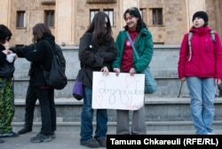 Holding the sign, Natalie is wearing the green jacket