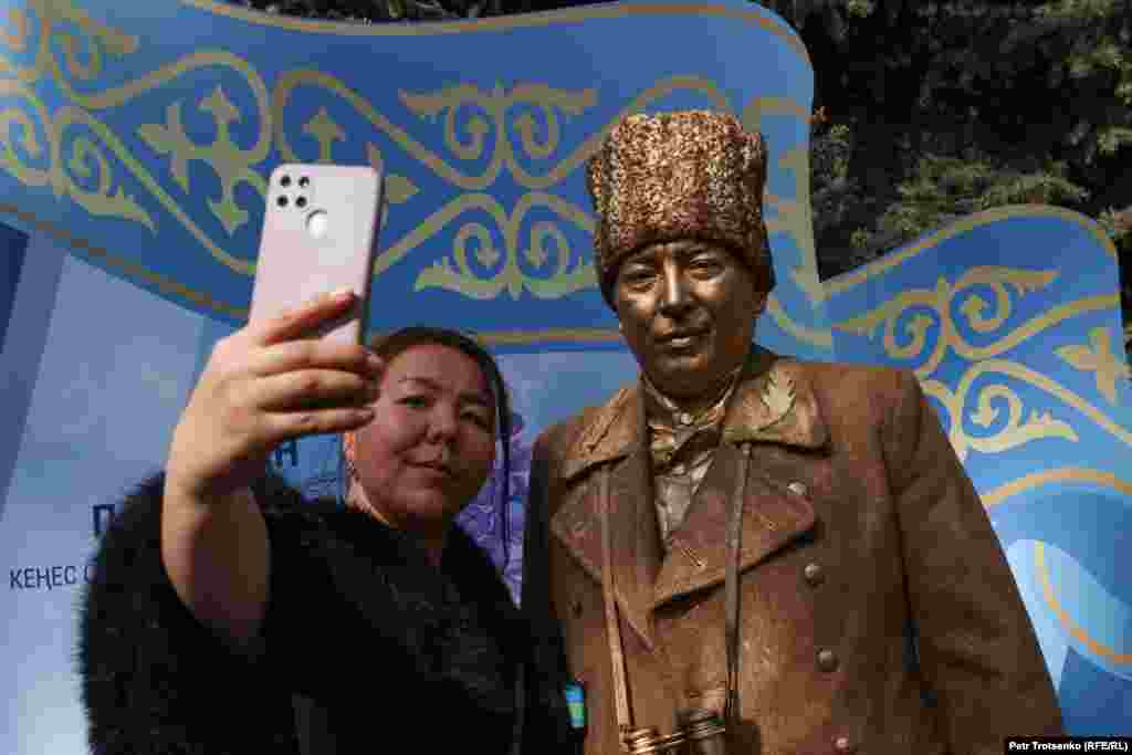 Женщина фотографируется с актёром, изображающим памятник писателю и участнику Второй мировой войны Бауыржану Момышулы
