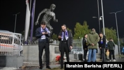 Dy tifozë izraelitë duke qëndruar pranë bustit të legjendës së futbollit shqiptar, Fadil Vokrri, pranë stadiumit i cili mban emrin e tij, para ndeshjes mes Kosovës dhe Izraelit në kualifikime për Euro 2024, 12 nëntor 2023.