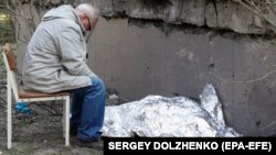 O rudă stă lângă cadavrul acoperit al unei tinere ucrainene care a fost ucisă într-un atac rusesc cu rachete asupra Kievului, pe 1 iunie.