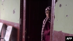 FILE: A Pakistani Kashmiri girl stands alongside a bullet-riddled wall of her house following the cross-border shelling in the village of Peer Klanjer in the Nakyal sector.