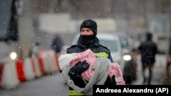 Një zjarrfikës mban një foshnje duke ikur nga Ukraina drejt Rumanisë.