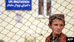 په کندهار کې یو ماشوم هېواد ته تر ستنېدو وروسته د مهاجرت نړیوال سازمان له دفتر سره ولاړ دی - د اپرېل اوومې انځور.