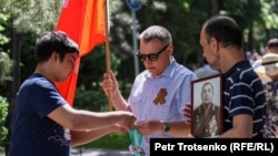 Георгий лентасын тагынган адамга көк лентаны сунуштап жаткан адам. Алматы, 9 май, 2022 жыл.