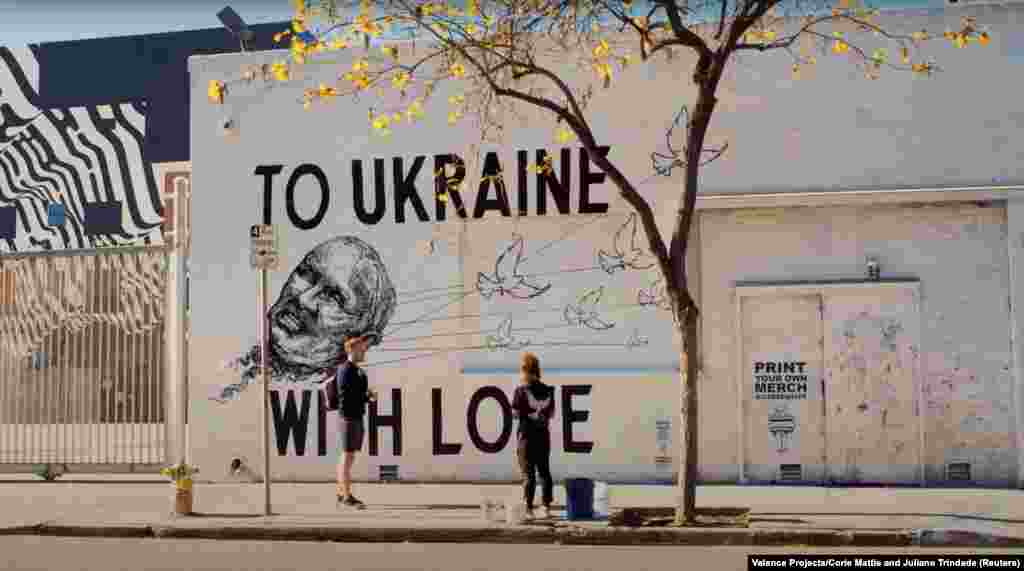 Artiștii Juliano Trindade și Corie Mattie de la Valence Projects stau în fața picturii lor Din Ucraina, cu dragoste, din Los Angeles. Pe 8 mai. Mattie a declarat pentru RFE/RL că este important să arăți un semn de speranță cu porumbeii luând puterea lui Putin.&nbsp;&bdquo;Cred că arta poate face diferența&rdquo;, a spus ea.&nbsp;&bdquo;Îi face pe privitori să se gândească la situațiile actuale, să schimbe perspectivele și chiar să îi determine pe oameni să acționeze.&rdquo;&nbsp;Această pictură murală are un cod QR care merge la banca națională a Ucrainei, care a înființat un fond pentru a strânge bani pentru trupele ucrainene.&nbsp;&bdquo;Este important să oferim oamenilor acces la activism&rdquo;, a spus Mattie.&nbsp;&bdquo;Arta bună te face să gândești, dar arta mare te face să faci.&rdquo;