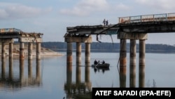Civilians cross the Siverskiy Donets River by boat under a damaged bridge in the liberated city of Stariy Saltiv east of Kharkiv. It's estimated that Ukraine will need hundreds of billions of dollars over the next 10 years to rebuild its devastated economy and infrastructure. (file photo)