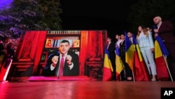 George Simion (AUR) transmite mesajul victoriei în primul tur al alegerilor prezidențiale, de la un birou având în fundal o bibliotecă cu icoane. Nu a venit în fața jurnaliștilor și a colegilor. Cuvintele sale au fost înregistrate și difuzate la ora exit-poll-urilor. 