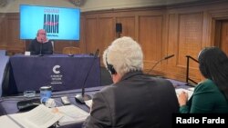 نمایی از یکی از جلسات دادگاه بین‌المللی آبان با حضور یکی از شاهدان که برای حفظ امنیت چهره خود را پوشانده بود