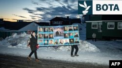 Dy burra në kryeqytetin e Grenlandës, Nuk, mbajnë një poster të madh për partinë Demokratike, e cila i fitoi zgjedhjet parlamentare të 11 marsit.