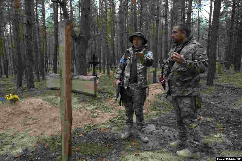 Oleg Kotenko, comisarul pentru problemele persoanelor dispărute în circumstanțe speciale, (stânga), vorbește cu camaradul său lângă mormintele neidentificate ale civililor și soldaților ucraineni din pădurea de lângă orașul Izium.&nbsp;Fotografie din 15 septembrie 2022.&nbsp;