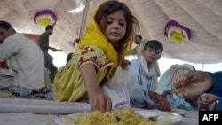 د بلوچستان په ډېره الله یار کې یوه سېلاب ځپلې ماشومه او نور کسان په کیمپ کې ډوډۍ خوري - د سېپټېمبر ۱۷مې انځور.