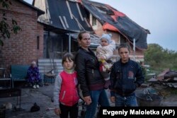 Margareta Tkacenko, la 29 de ani, împreună cu copiii ei, Sofia, Veronika și Nikita, în fața casei lor avariate din orașul Izium, recent recucerit, Ucraina, 25 septembrie 2022.