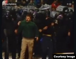 დაკავების კადრებში ჩანს, რომ კორდონიდან გამოსულ გიორგის სახე სისხლიანი აქვს, ტანსაცმელი სველი და გარშემო მხოლოდ ნიღბიანი პოლიციელები ჰყავს