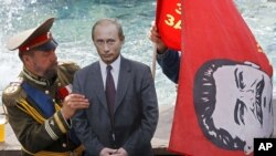 مردی در لباس و شمایل تزار نیکولای دوم، پیکره‌ای مقوایی از پوتین را در کنار پرچمی با نقش استالین قرار می‌دهد/ مسکو، ژوئیه ۲۰۱۲