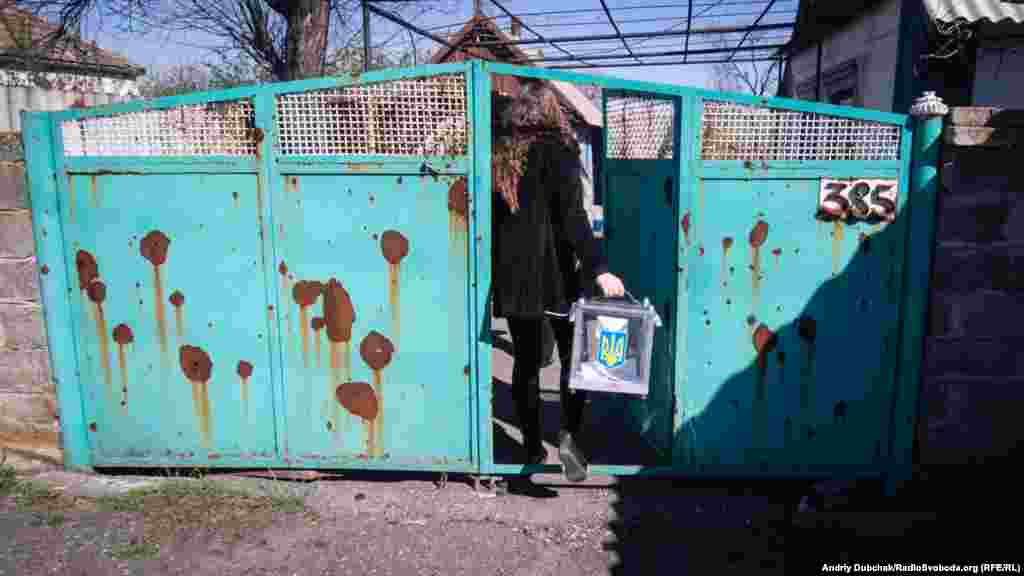 An election official brings a ballot box to the front-line village of Novotroitse in the Donetsk region on April 21. As the gates show, most homes here have been damaged by shelling.
