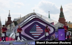 Учесниците настапуваат покрај екран на кој е прикажано знамето на Соединетите Американски Држави за време на церемонијата по повод 100-дневното одбројување до почетокот на Интервижн натпреварот за песна, во близина на Кремљ во центарот на Москва, Русија, на 12 јуни 2025 година.