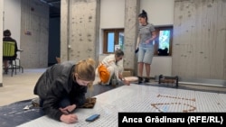 Regizoarea Chris Simion-Mercurian și două dintre colegele sale scriu pe o planșă numele celor care au donat pentru construirea teatrului Grivița 53. Numele lor vor fi afișate pe unul dintre pereții teatrului.