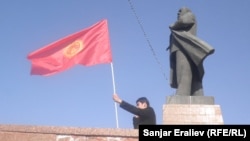 Un bărbat flutură un steag al Kârgâzstanului lângă o statuie a liderului sovietic Vladimir Lenin în centrul orașului Oș. Autoritățile orașului au dărâmat statuia în iunie 2025.