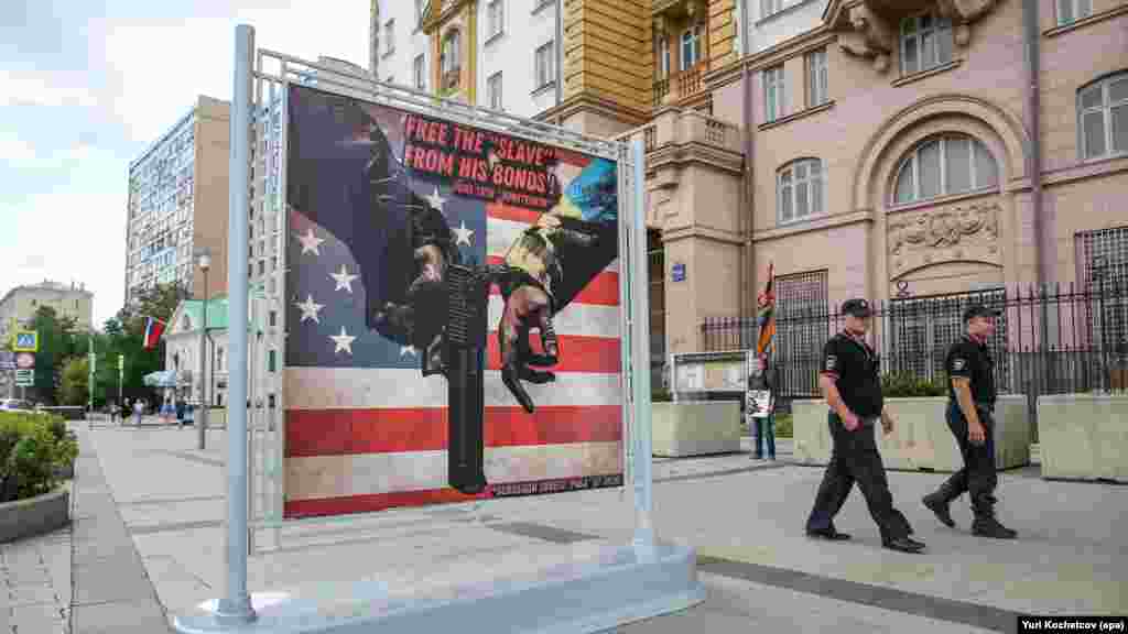 Русия също използва този подход. Това е кадър на двама полицаи, които минават покрай плакат, изобразяващ ръката на човек в костюм в цветовете на украинското знаме (вдясно), окован с белезници за ръката на друг човек, който държи американски пистолет Desert Eagle с надпис "Освободете "роба" от оковите му!", пред главната сграда на посолството на САЩ в Москва, Русия, 26 юни 2024 г.