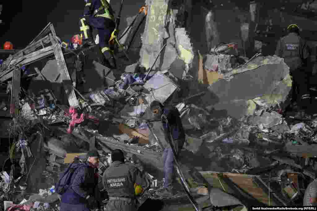 Shpëtimtarët punojnë në vendin e një ndërtese banimi të goditur nga një raketë balistike ruse në Kiev.Ata nxituan për t'i nxjerrë të mbijetuarit nga rrënojat e ndërtesës, duke i dëgjuar tingujt e telefonave celularë, në përpjekje për t'i gjetur ata.