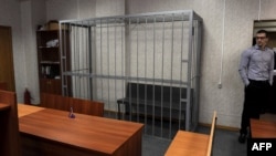 An employee stands near the empty defendant's dock in the Tverskoi district court in Moscow where the posthumous trial of Sergei Magnitsky was begun and immediately postponed for 10 days on March 11.