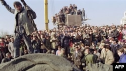 A man stands atop a statue of Soviet leader Vladimir Lenin after it was removed from its pedestal in Bucharest on March 5, 1990.