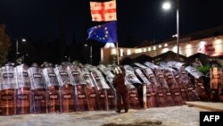 Un protestatar, fluturând steagurile Georgiei și Uniunii Europene în fața unmui cordon de polițiști, la Tbilisi , pe 4 octombrie 2025