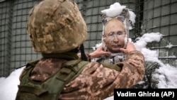 Një ushtar ukrainas heq borën nga një portret i presidentit rus, Vladimir Putin,  në rajonin Luhansk, në lindje të Ukrainës. 

